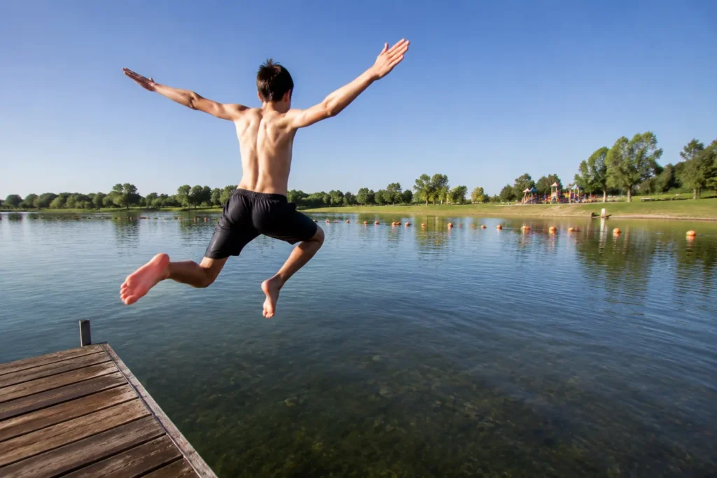 The best swimming lake near me in Colorado. Boy jumping off dock into Big Soda Lake at Bear Creek Lake Park in Lakewood, Colorado.