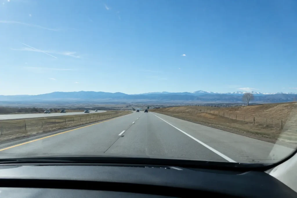 Car driving west on I-70 from Denver toward the Colorado mountains under a clear sky